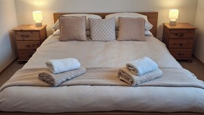 Een net opgemaakt bed met twee kussens, een nachtkastje met een lamp, en drie ingelijste foto's aan de muur.