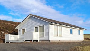 Een gelijkvloers wit huis met een veranda, grote ramen en een schuin dak.