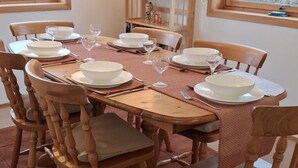 Een eettafel gedekt met witte borden, kommen en wijnglazen, omringd door houten stoelen met beklede zitplaatsen.
