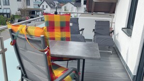 En balkong med ett metallbord och två stolar, var och en med färgglada kuddar.