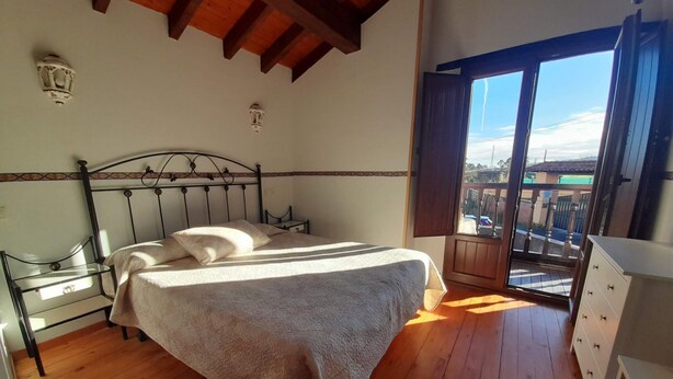 Ein Schlafzimmer mit Bett, Nachttischen, einem Schminktisch und einem großen Fenster mit Blick ins Freie.