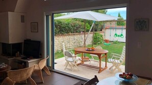 A modern living room with a television, dining area, and large sliding glass door leading to a garden. - La Venelle de Cali - Large Home with 3 Separate Units (Île-d'Aix)