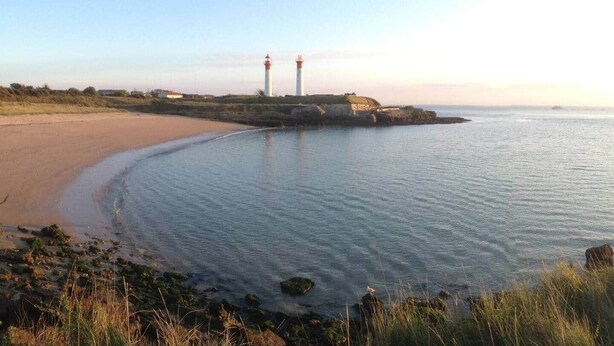 A coastal scene with a sandy beach, calm waters, and two lighthouses in the distance. - La Venelle de Cali - Large Home with 3 Separate Units (Île-d'Aix)