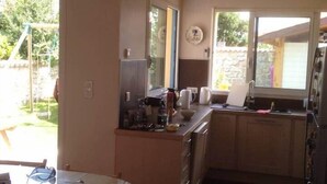 A compact kitchen with a round table and chairs, a refrigerator, and a window overlooking a garden. - La Venelle de Cali - Large Home with 3 Separate Units (Île-d'Aix)
