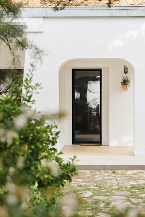 A white building with a black-framed door, a small potted plant, and a lantern on the wall. - Kallisté - Stunning Oceanview Villa (Île-d'Aix)