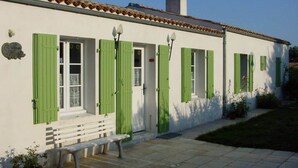 A white building with green shutters, a chimney, and a bench outside. - La Léinade - Spacious Family Villa (Île-d'Aix)