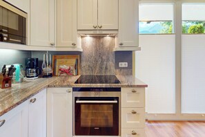 Une cuisine avec des meubles blancs, un plan de travail en granit, un four Siemens et une vue sur la verdure grâce à une porte coulissante.