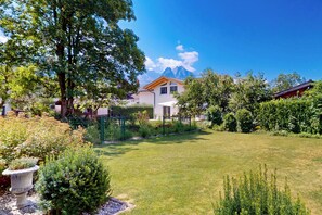 A residential property with a well-maintained lawn, a stone fountain, and a mountain view in the background. - Vacation apt. Verena in Garmisch – stylish, central, and with green garden oasis (Garmisch-Partenkirchen)