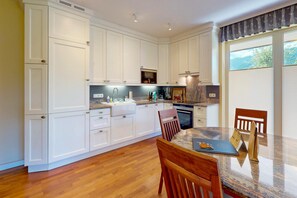 A modern kitchen with white cabinetry, a granite countertop, and a dining area with a table and chairs. - Vacation apt. Verena in Garmisch – stylish, central, and with green garden oasis (Garmisch-Partenkirchen)