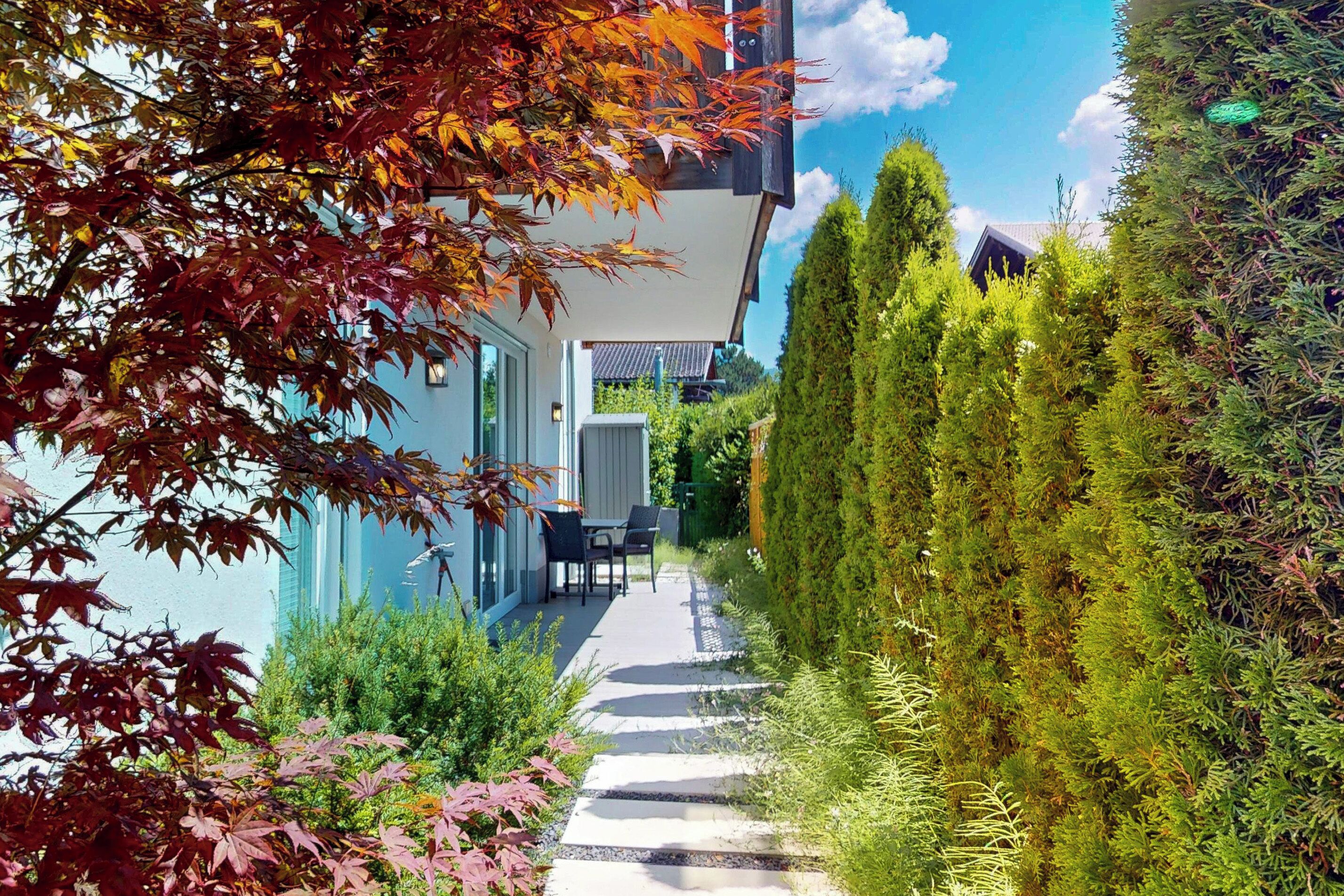 A modern building with a glass facade, a paved pathway, and a neatly trimmed hedge.