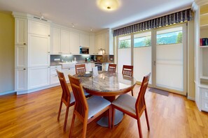 A modern kitchen with white cabinetry, a granite countertop, and a dining area with a round table and wooden chairs. - Vacation apt. Verena in Garmisch – stylish, central, and with green garden oasis (Garmisch-Partenkirchen)