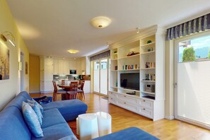 A modern living room with a blue sofa, a flat-screen TV, and a bookshelf. - Vacation apt. Verena in Garmisch – stylish, central, and with green garden oasis (Garmisch-Partenkirchen)
