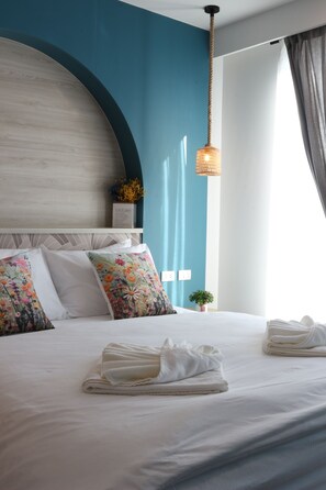 A neatly made bed with floral pillows, a small plant, and a hanging light fixture in a room with teal walls and a white headboard. - J The Park Condotel (Hat Yai)