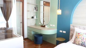A modern bedroom with a large bed, a vanity with a mirror, a small stool, and a blue trash bin.