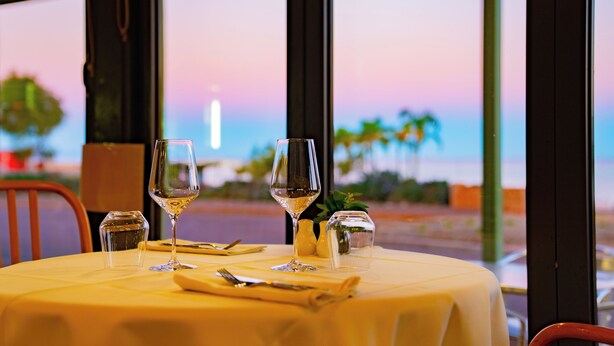 A table set for dining with a view of the sunset through large windows. - The Beach Hotel Whyalla (Whyalla)