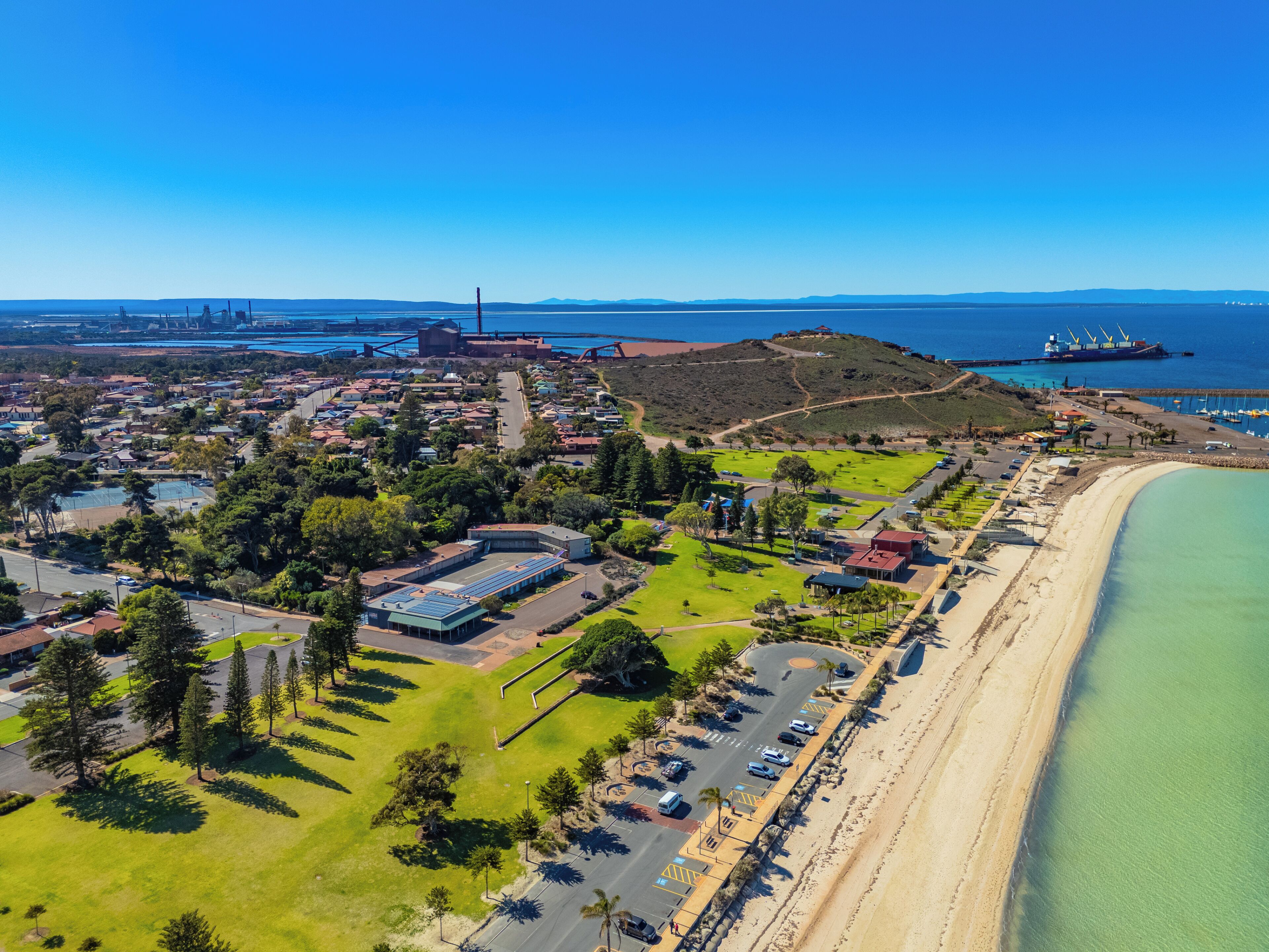 An aerial view of a coastal town with a beach, residential areas, and industrial structures.