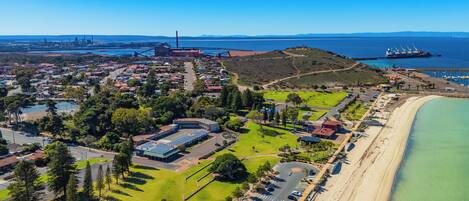 An aerial view of a coastal town with a beach, residential areas, and industrial structures.