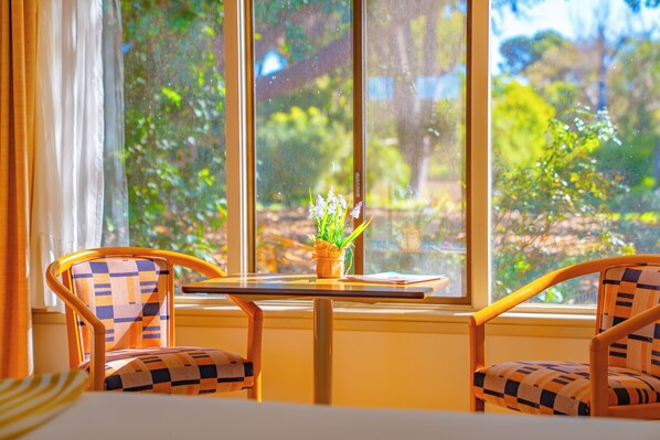A room with two patterned chairs, a small table, and a window with a view of greenery. - The Beach Hotel Whyalla (Whyalla)