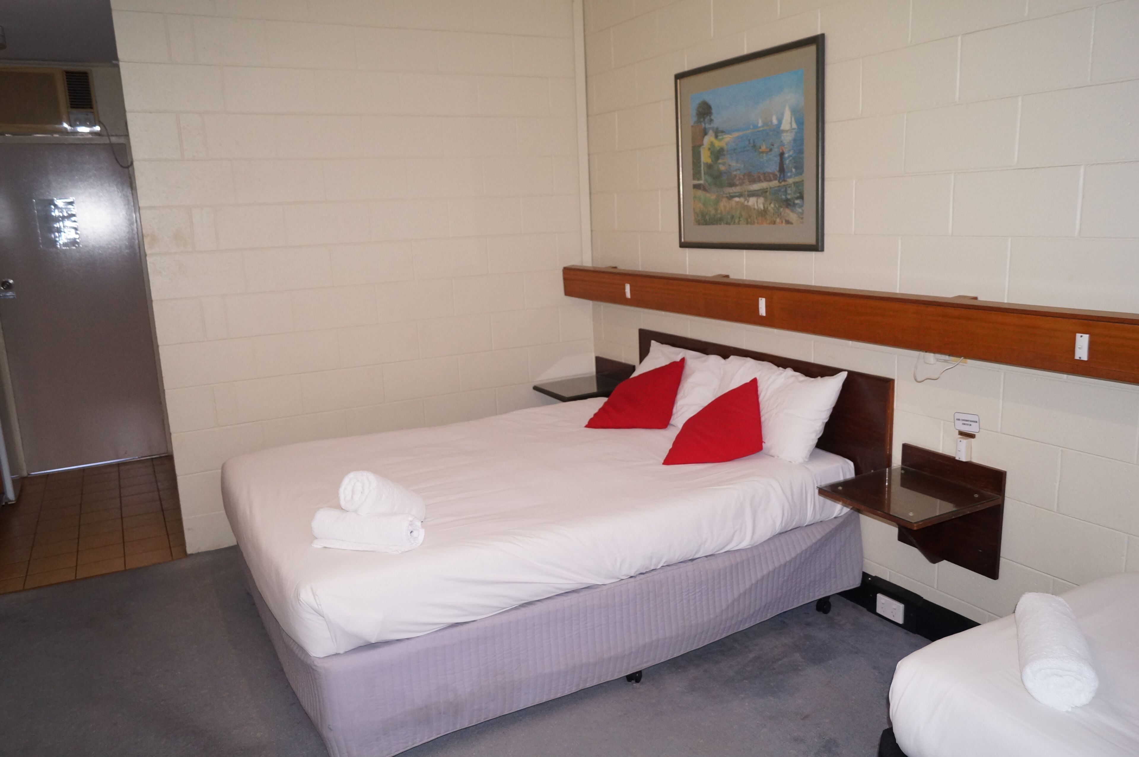 A hotel room with a bed, a nightstand, a painting on the wall, and a door.