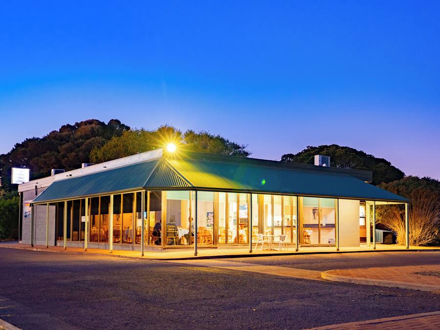 A modern building with a glass facade and a green roof, likely a restaurant or cafe, with outdoor seating visible.