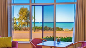 A room with a large window overlooking a beach, a table, and a purple chair. - The Beach Hotel Whyalla (Whyalla)