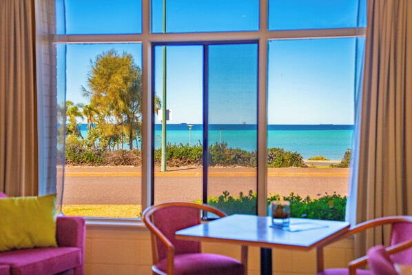 Ein Zimmer mit großem Fenster und Meerblick, einem Tisch und einem violetten Sessel.