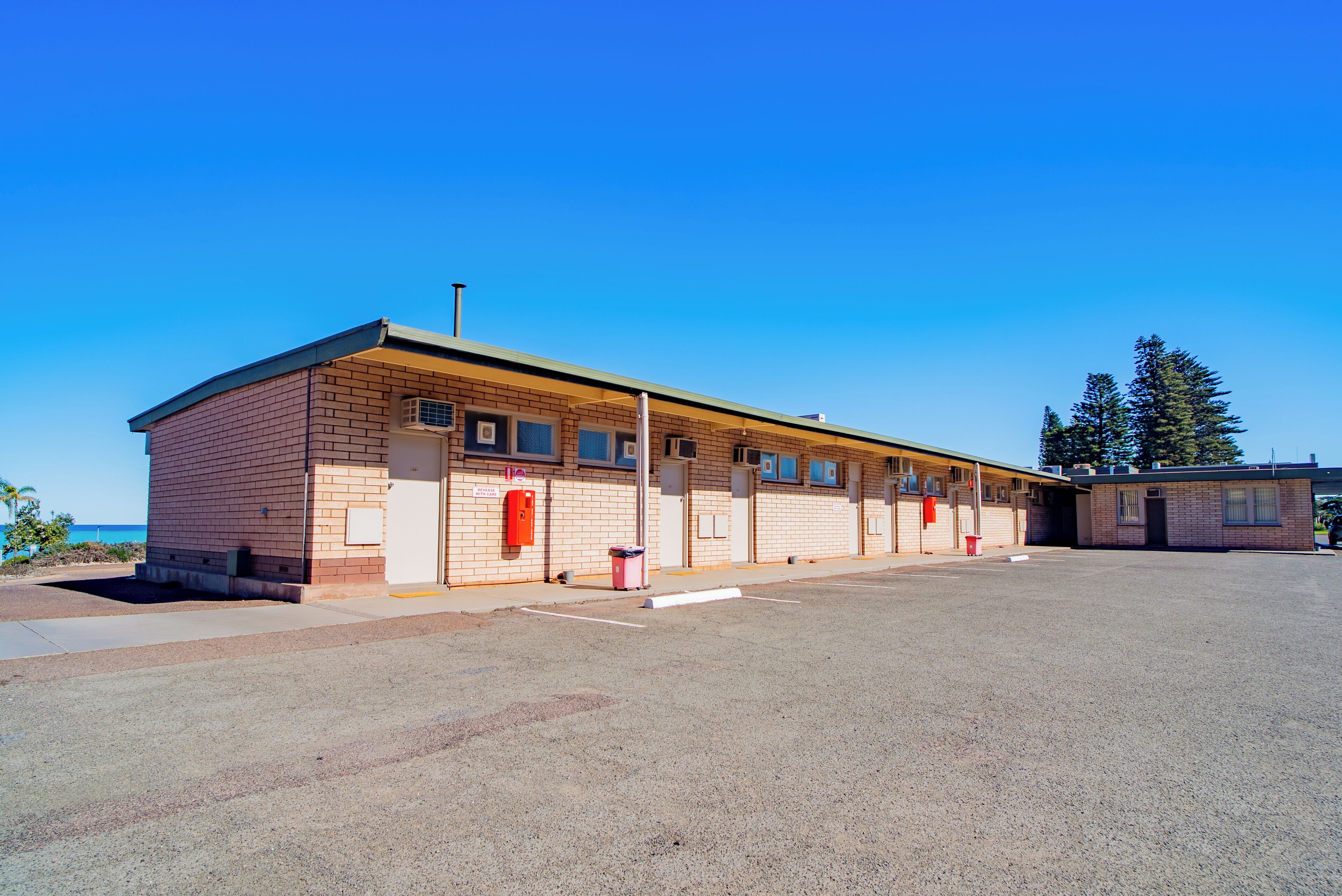 A single-story brick building with a flat roof, a covered parking area, and a clear blue sky.