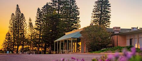 A building with a covered patio area, surrounded by tall trees and a parking lot.