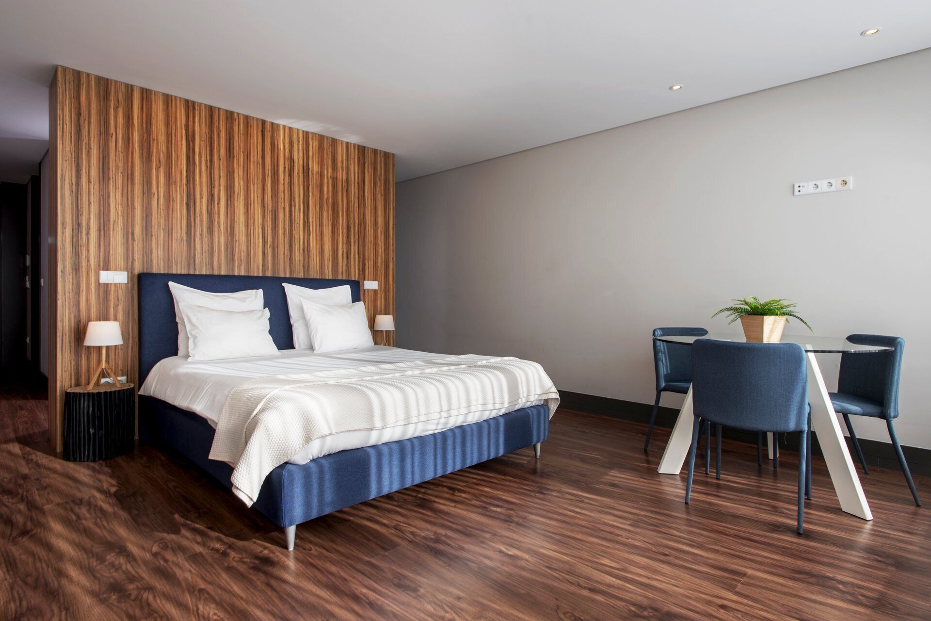 A modern hotel room with a large bed, a small table with chairs, and a potted plant.
