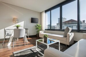 A modern living room with a sofa, a coffee table, a TV, and large windows. - Guestready - Bahl Apartments (Porto)