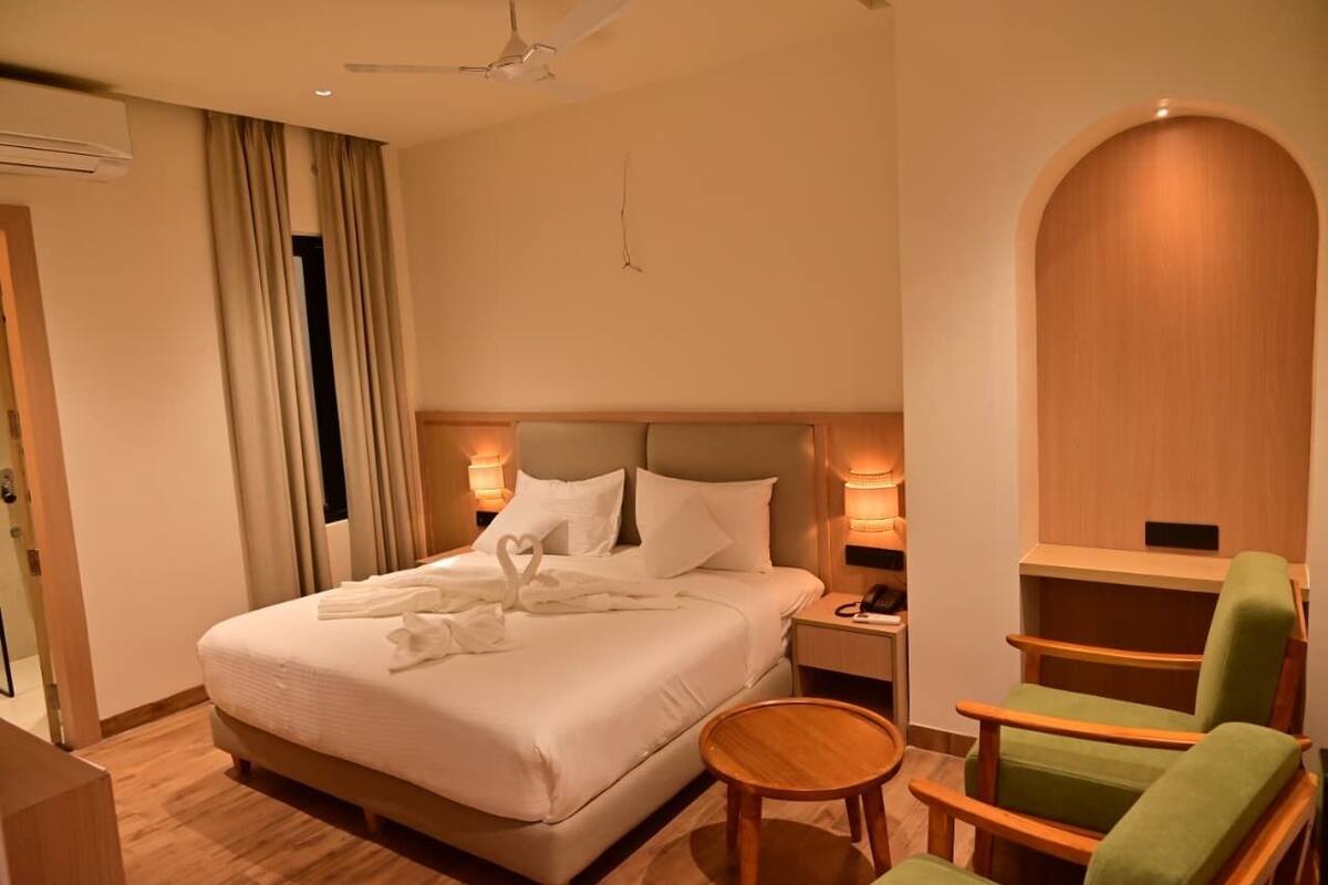 A hotel room with a bed, a nightstand, a green chair, and a wooden side table.
