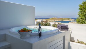 A hot tub with a view of the sea, a basket of fruit, and a bottle of wine on a balcony. - Villa Nikolas, pool and jacuzzi - My Rental Homes (Mykonos)