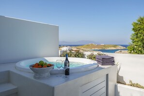 Ein Whirlpool mit Meerblick, ein Obstkorb und eine Weinflasche auf einem Balkon.