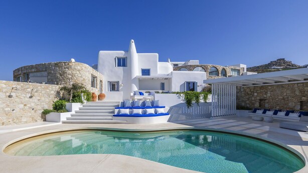 A modern white building with a pool, stone walls, and blue accents. - Villa Nikolas, pool and jacuzzi - My Rental Homes (Mykonos)