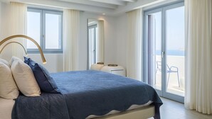 A bedroom with a bed, a nightstand, and a view of the sea through large windows. - Villa Nikolas, pool and jacuzzi - My Rental Homes (Mykonos)