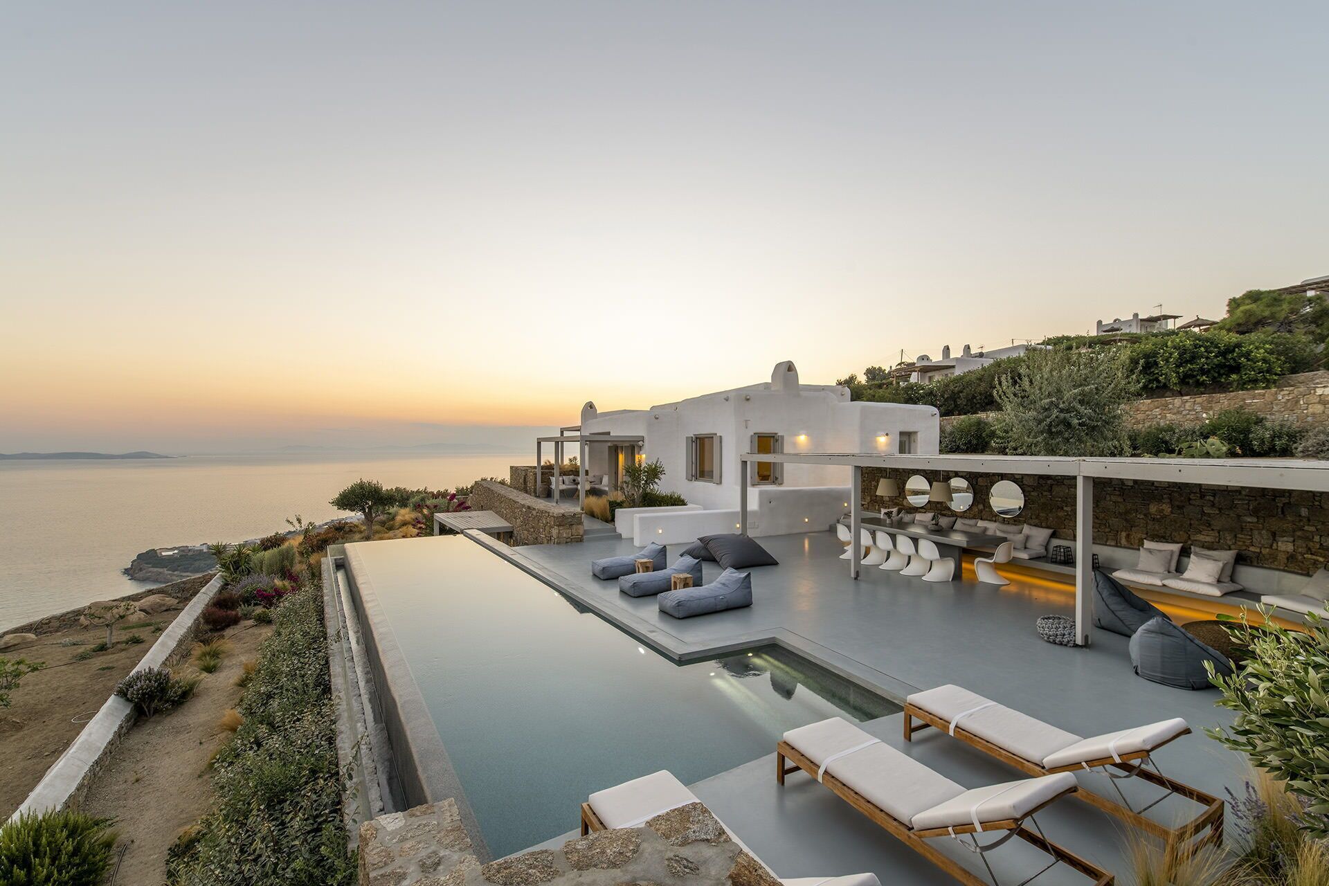 A modern outdoor pool area with lounge chairs and a dining setup overlooking the sea.