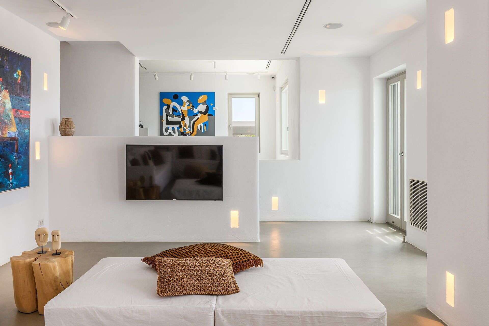 Une chambre d’hôtel moderne dotée d’un grand téléviseur à écran plat fixé au mur, d’un lit avec du linge de lit blanc et d’un plaid en tissu tissé.