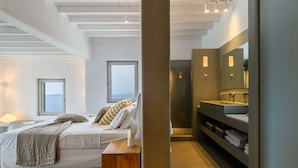 Quarto moderno com cama, mesa de cabeceira e vista para o mar.