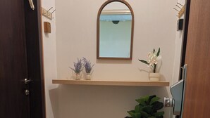 Un baño con espejo, estante con plantas, una maceta y una puerta.