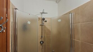 Un espacio de ducha pequeño y cerrado con puerta de cristal, un cabezal de ducha manual y un grifo instalado en la pared.