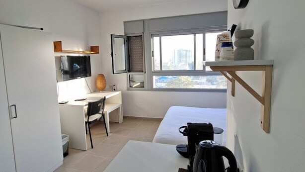 Una habitación de hotel moderna con escritorio, silla, cama y cafetera sobre la mesa.