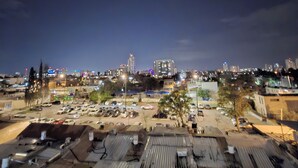 Un paisaje urbano nocturno con una mezcla de edificios residenciales y comerciales, incluyendo un estacionamiento con varios automóviles.