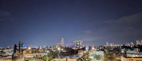 A nighttime cityscape with a mix of residential and commercial buildings, including a parking lot with several cars.