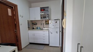 Cocina compacta con armarios blancos, un refrigerador con una calcomanía y un pequeño comedor con mesa y sillas.