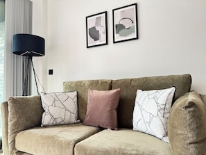 A beige sectional sofa with patterned cushions, a black floor lamp, and abstract artwork on the wall. - 2 Bed Flat - Sleeps 4 - Parking - Wifi (Manchester)