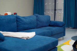 A blue sofa in a modern living room with a glass door and blue curtains.