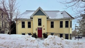 A yellow building with a red door, multiple windows, and a snow-covered roof. - 3BR Condo |  Bayfield Lake Views (Bayfield)