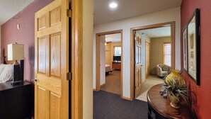 A hotel room with a wooden door, a desk with a lamp, a bed, a small table with a vase, and a framed picture on the wall. - 3BR Condo |  Bayfield Lake Views (Bayfield)