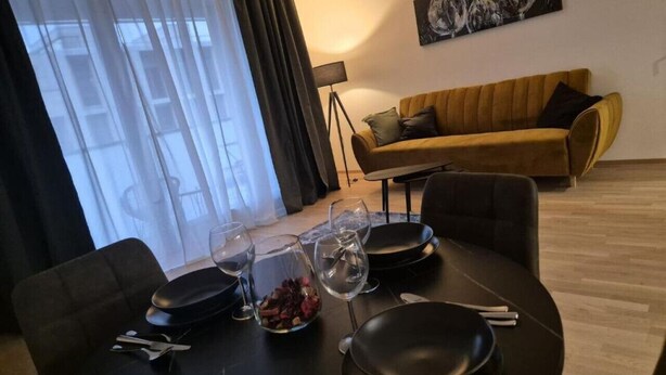 Ruokailutila, jossa on kahdelle katettu pöytä, hedelmäkulho ja viinilaseja. Taustalla on sohva ja lamppu.
