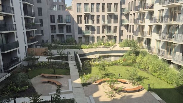 A modern apartment complex with multiple balconies, a central courtyard with greenery, and a mix of residential and commercial buildings in the background. - Smichov Luxury apartments (Prague 5)